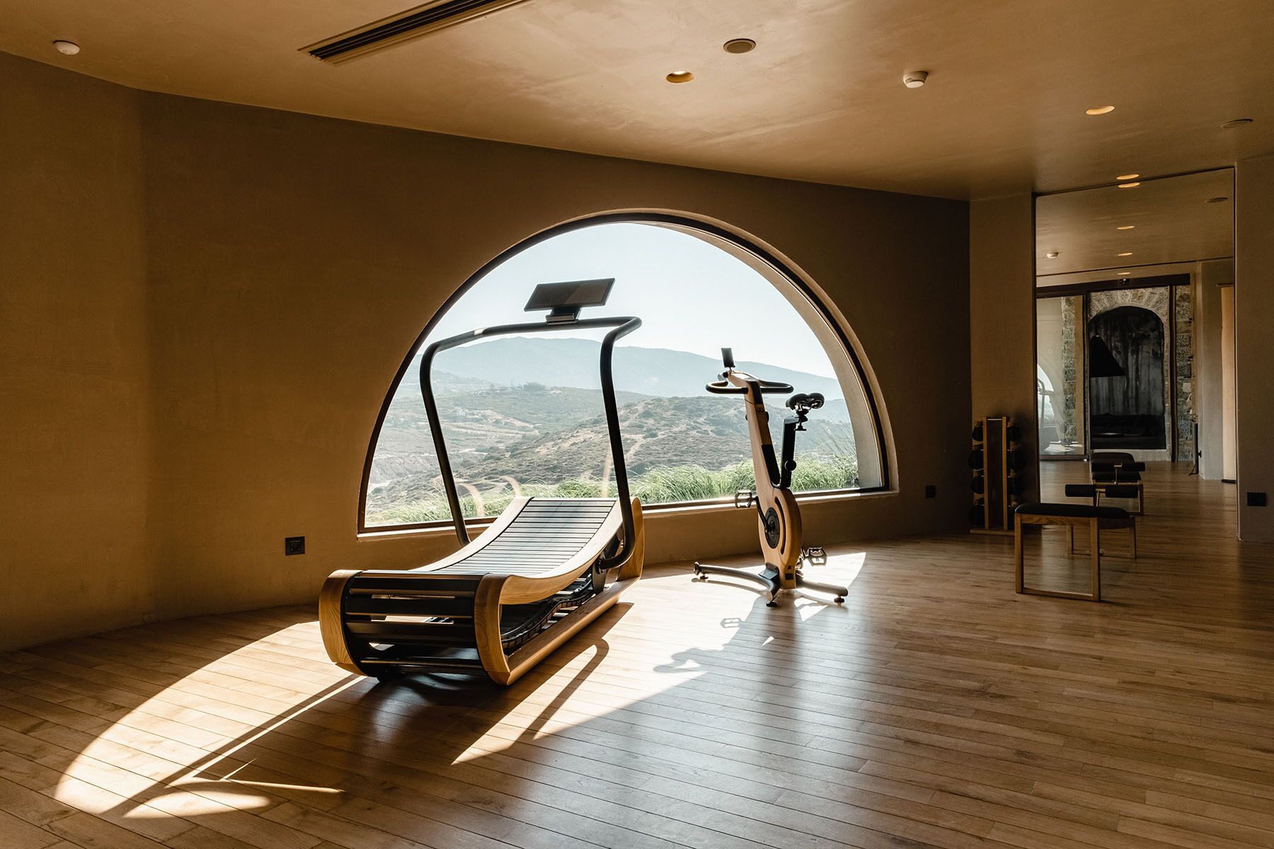 A spacious room with a large arched window offering a view of a mountainous landscape.