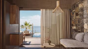 A modern room with a stone wall, a view of the ocean, a sofa, a small table with a vase, and a hanging light fixture.