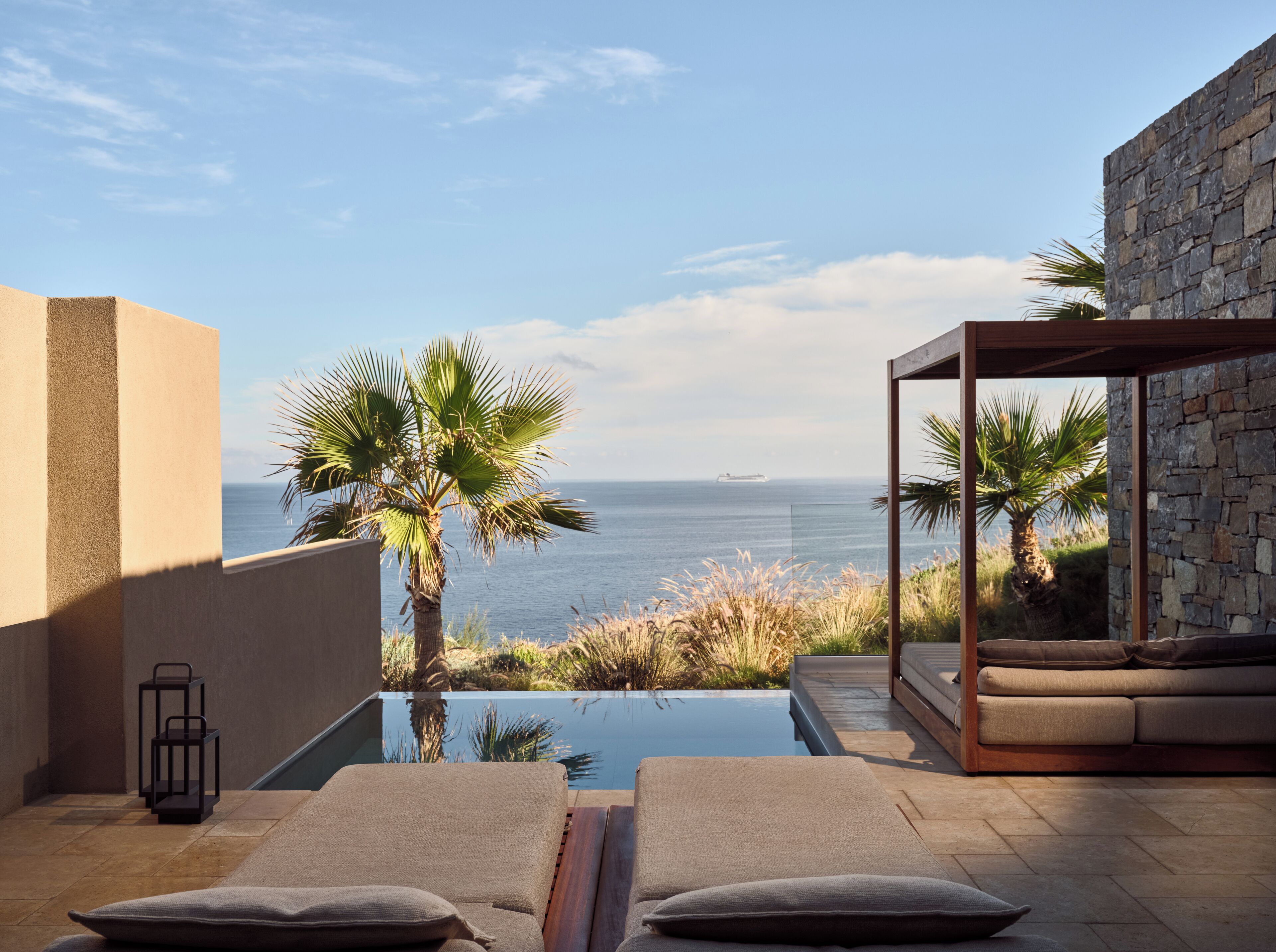 Een balkon met uitzicht op zee, een zwembad, ligstoelen en een stenen muur.