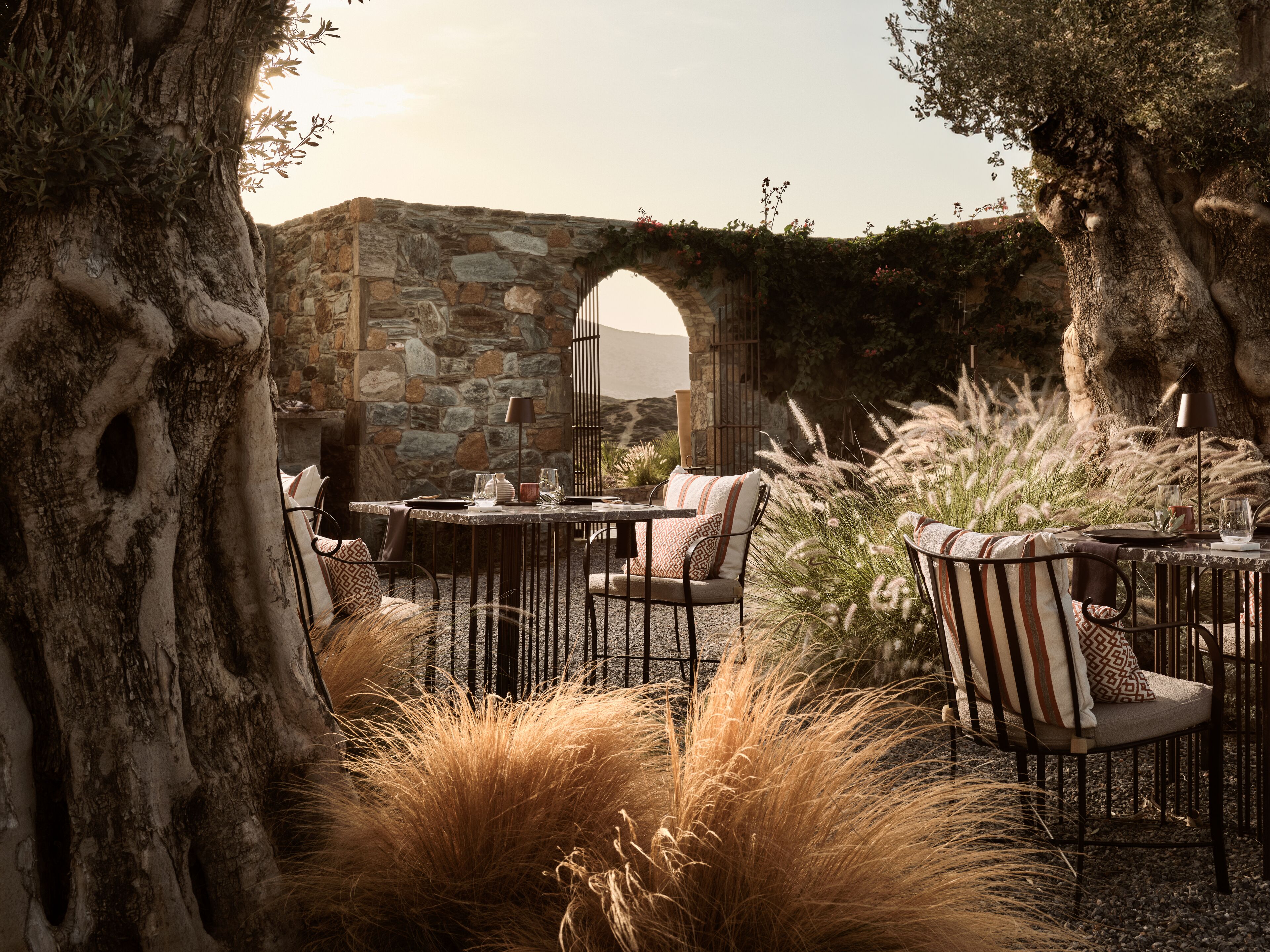 An outdoor seating area with stone walls, a table, chairs, and tall grasses.