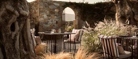 An outdoor seating area with stone walls, a table, chairs, and tall grasses.