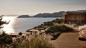 A coastal resort with a wooden deck, outdoor seating, and a view of the sea and hills. - Acro Wellness Suites - Adults Only (Malevizi)