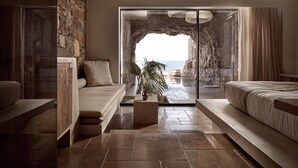 A modern bedroom with a stone wall, a large window, and a view of the sea. - Acro Wellness Suites - Adults Only (Malevizi)