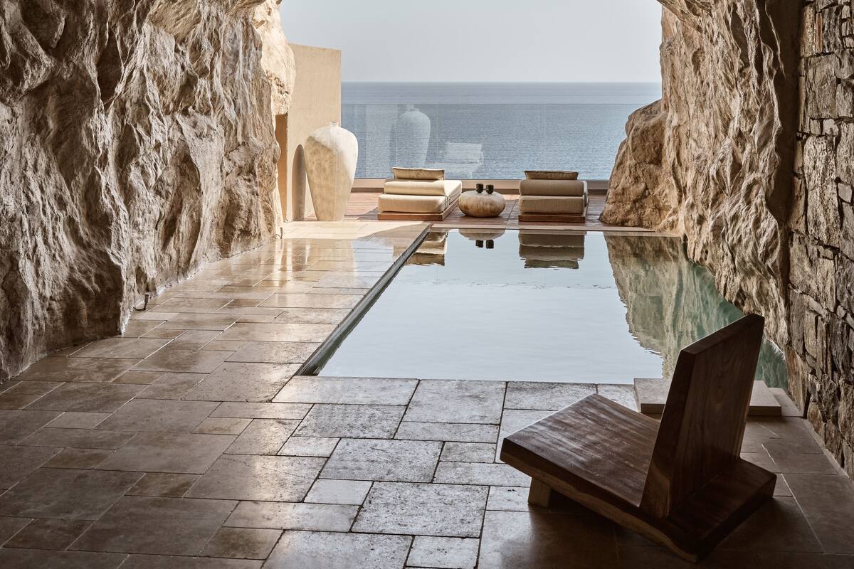 A modern infinity pool with a clear view of the sea, stone walls, and minimalist furniture.