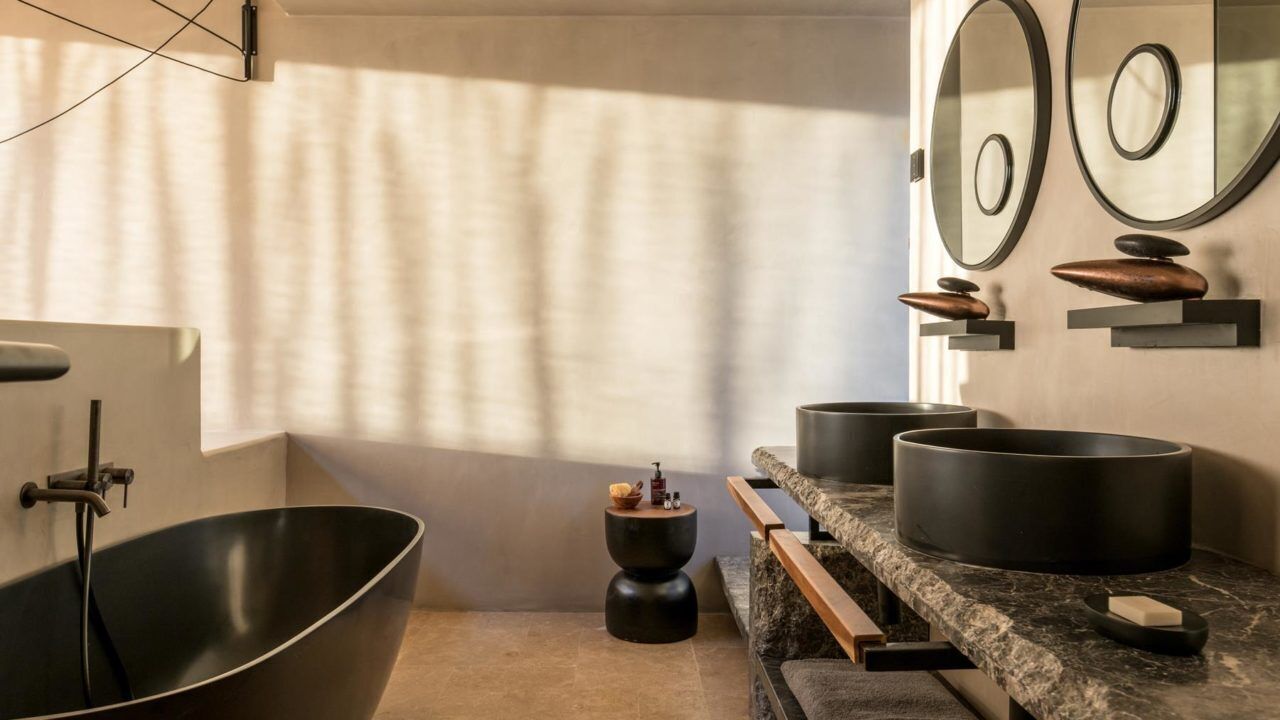 A modern bathroom with a freestanding bathtub, a marble vanity with black pots, and a small round table with toiletries.