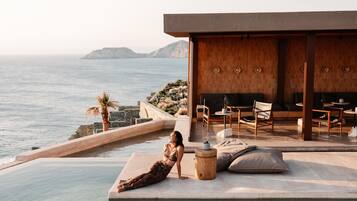 Un espace aménagé au bord de la piscine, avec vue sur la mer, une terrasse en bois et un coin salon comprenant un canapé et des fauteuils.