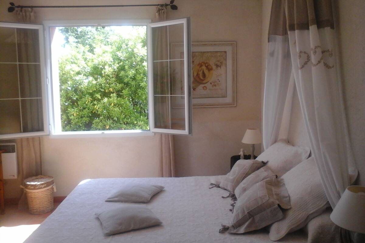 Een slaapkamer met een bed, een raam met open gordijnen, een bedlamp en een lijst met een afbeelding aan de muur.