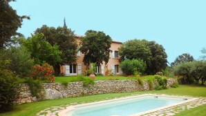 A pool surrounded by a stone wall, with a grassy area and trees.