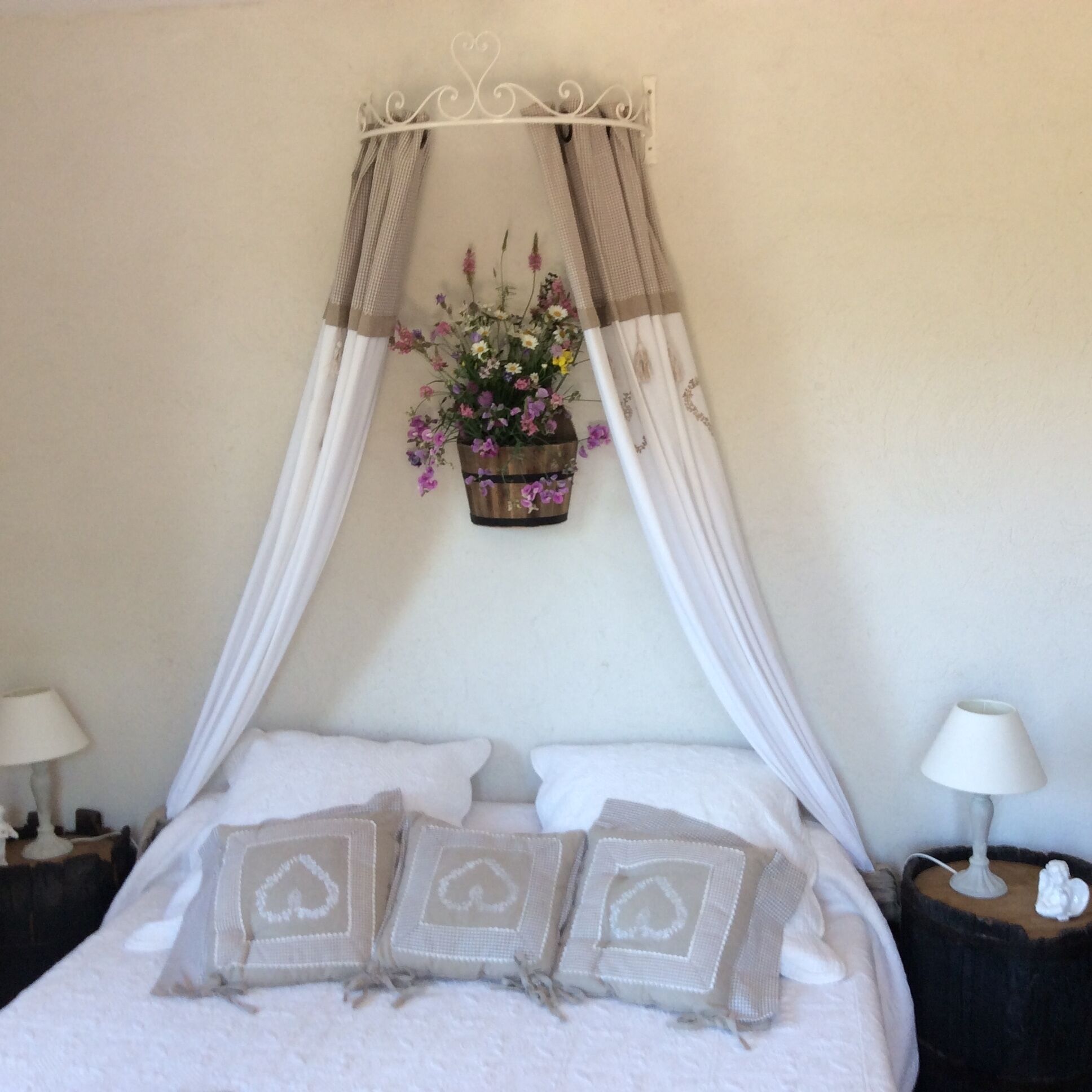 Een bed met een hemelbed, witte kussens en een bloemenmandje.