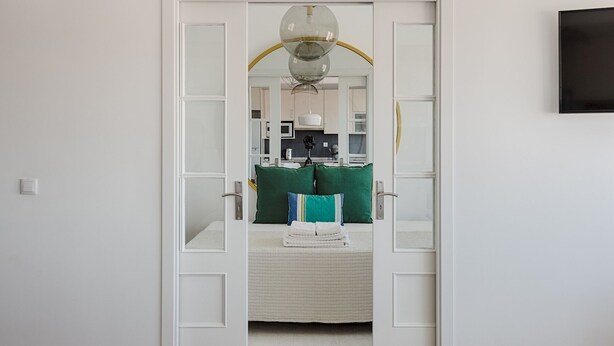 A hallway leading to a bedroom with a bed, a small table, and a green chair. - Master Deco Gem in Graça (Lisboa)