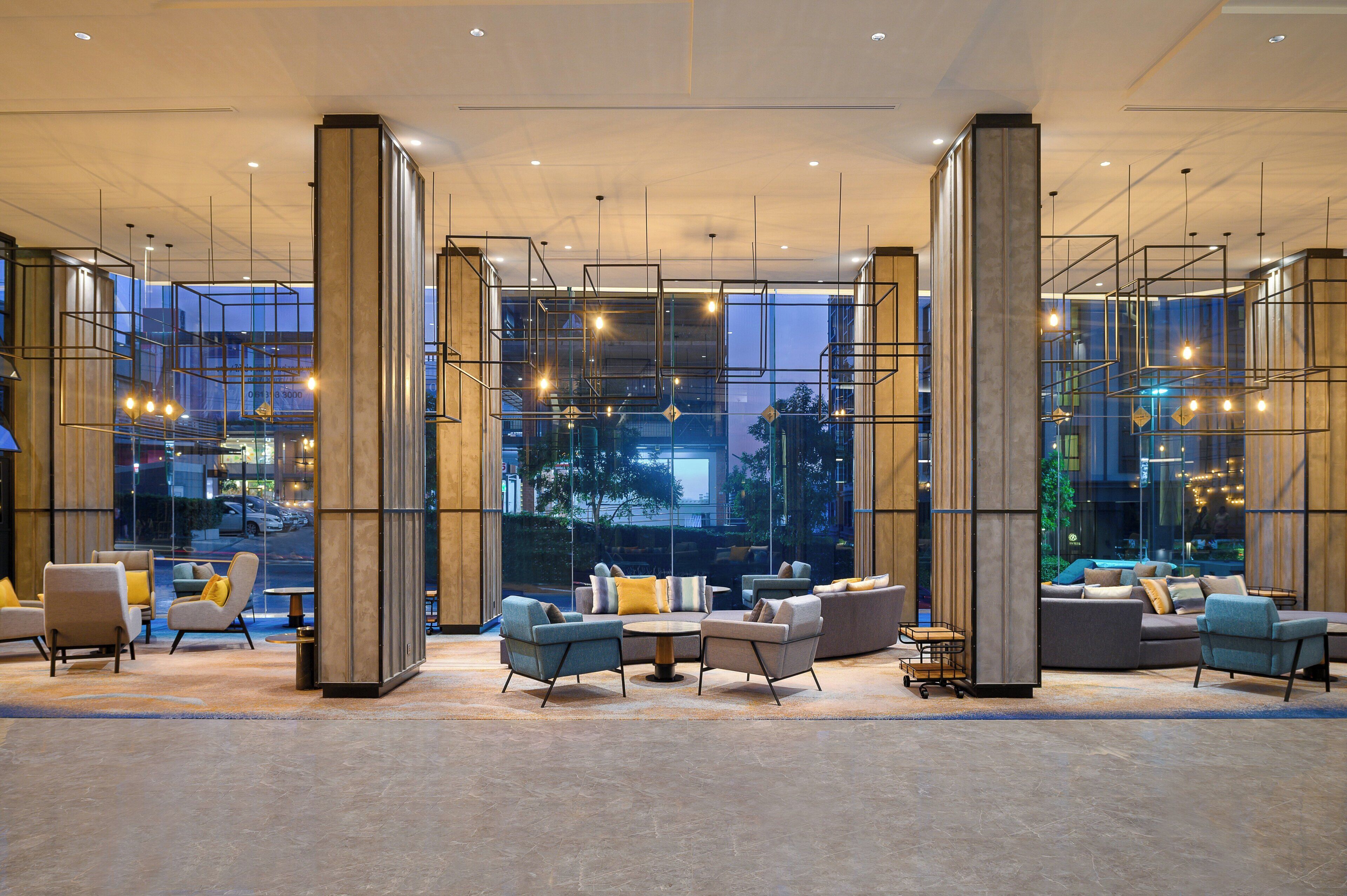 A modern lobby with a seating area, large windows, and hanging light fixtures.