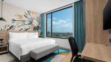 Habitación de hotel con una cama grande, un escritorio, una silla, vistas a la ciudad y un colorido mural abstracto.