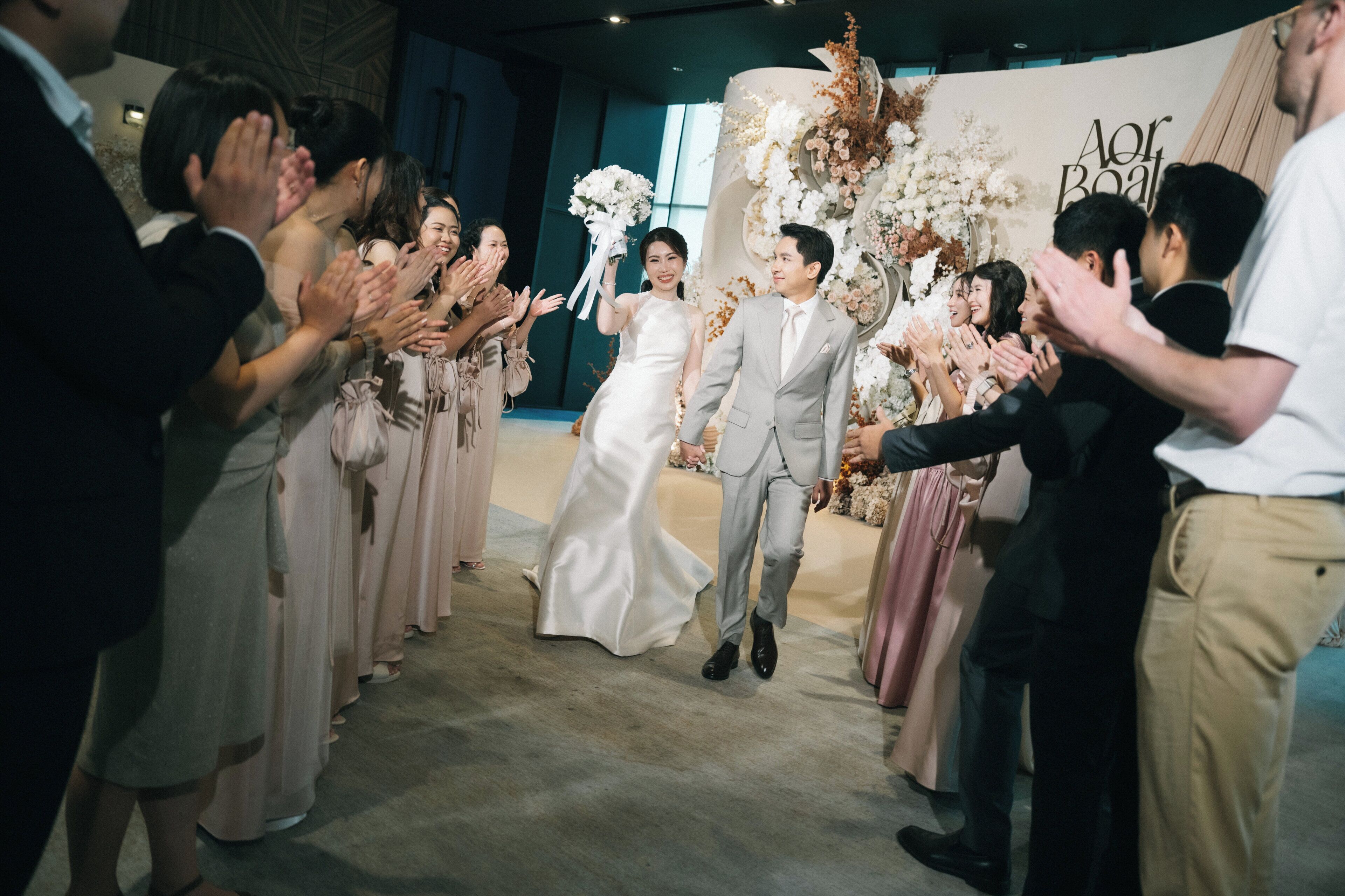 A wedding ceremony with guests clapping, a couple in wedding attire, and a floral backdrop.