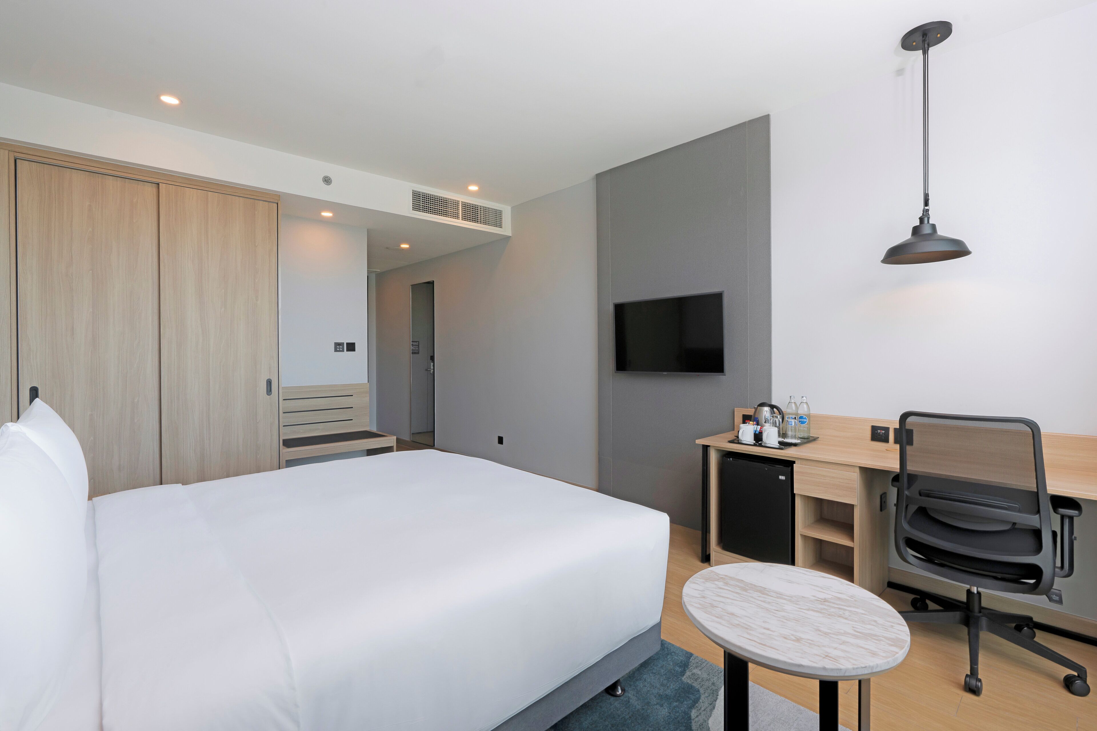 A hotel room with a bed, desk, chair, TV, and wardrobe.