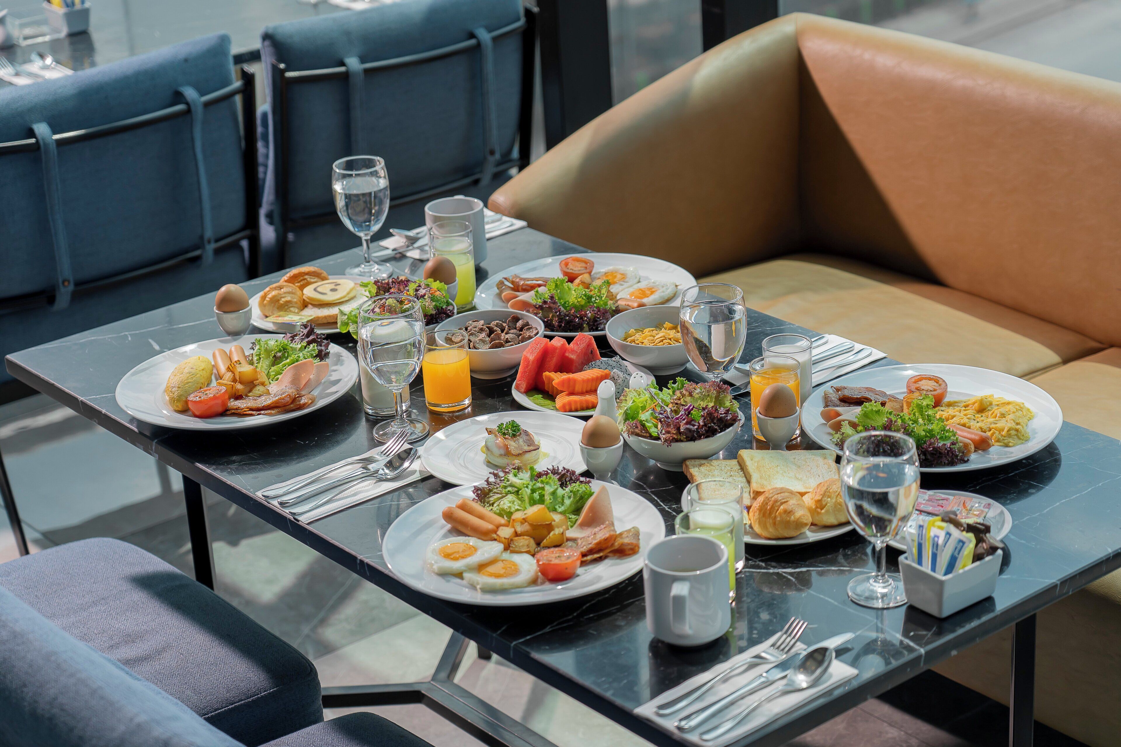 A breakfast table with plates of food, glasses of water, and a bowl of salad.