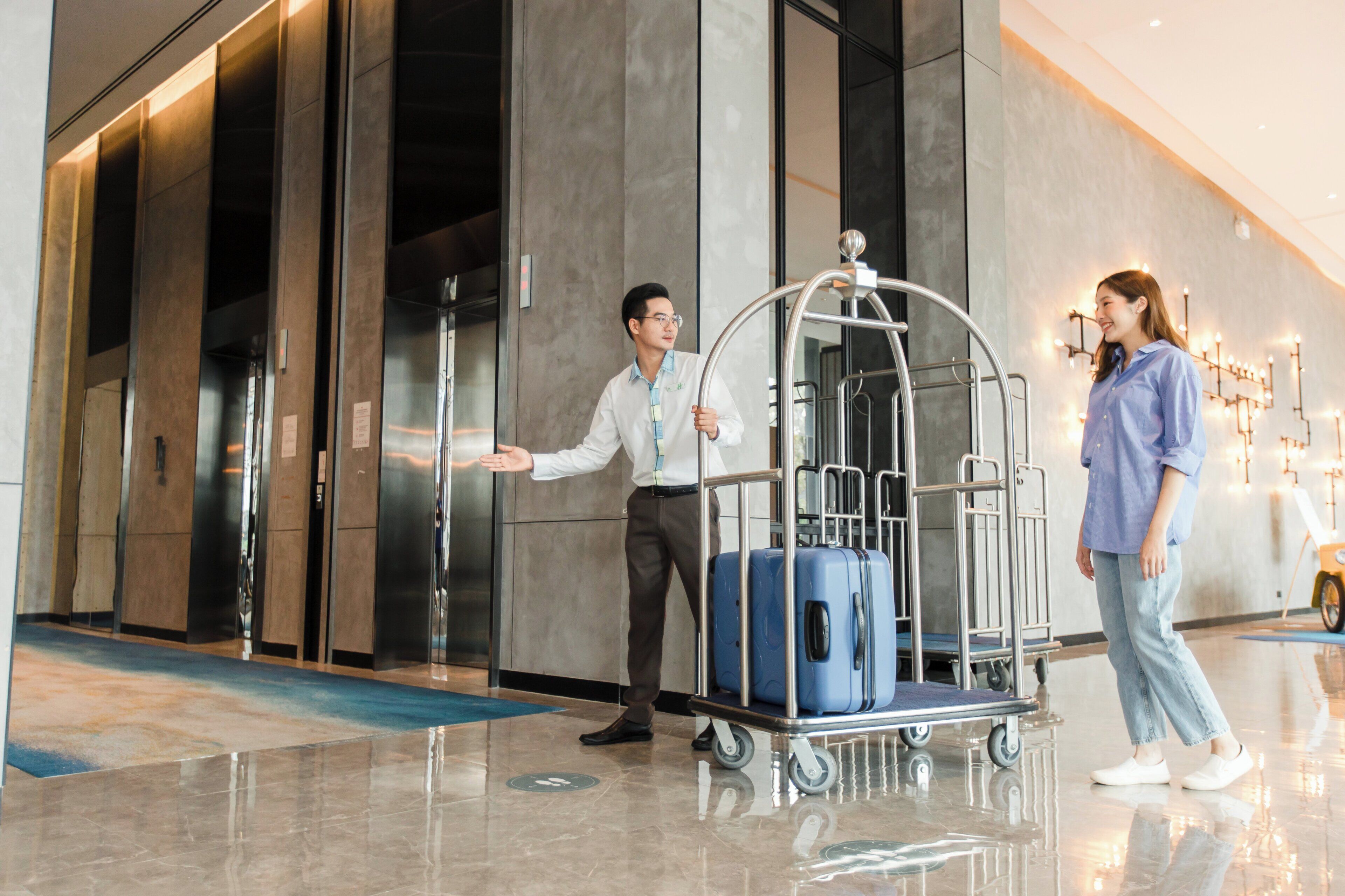 A hotel lobby with a luggage cart, a man in a white shirt, and a woman in a blue shirt.