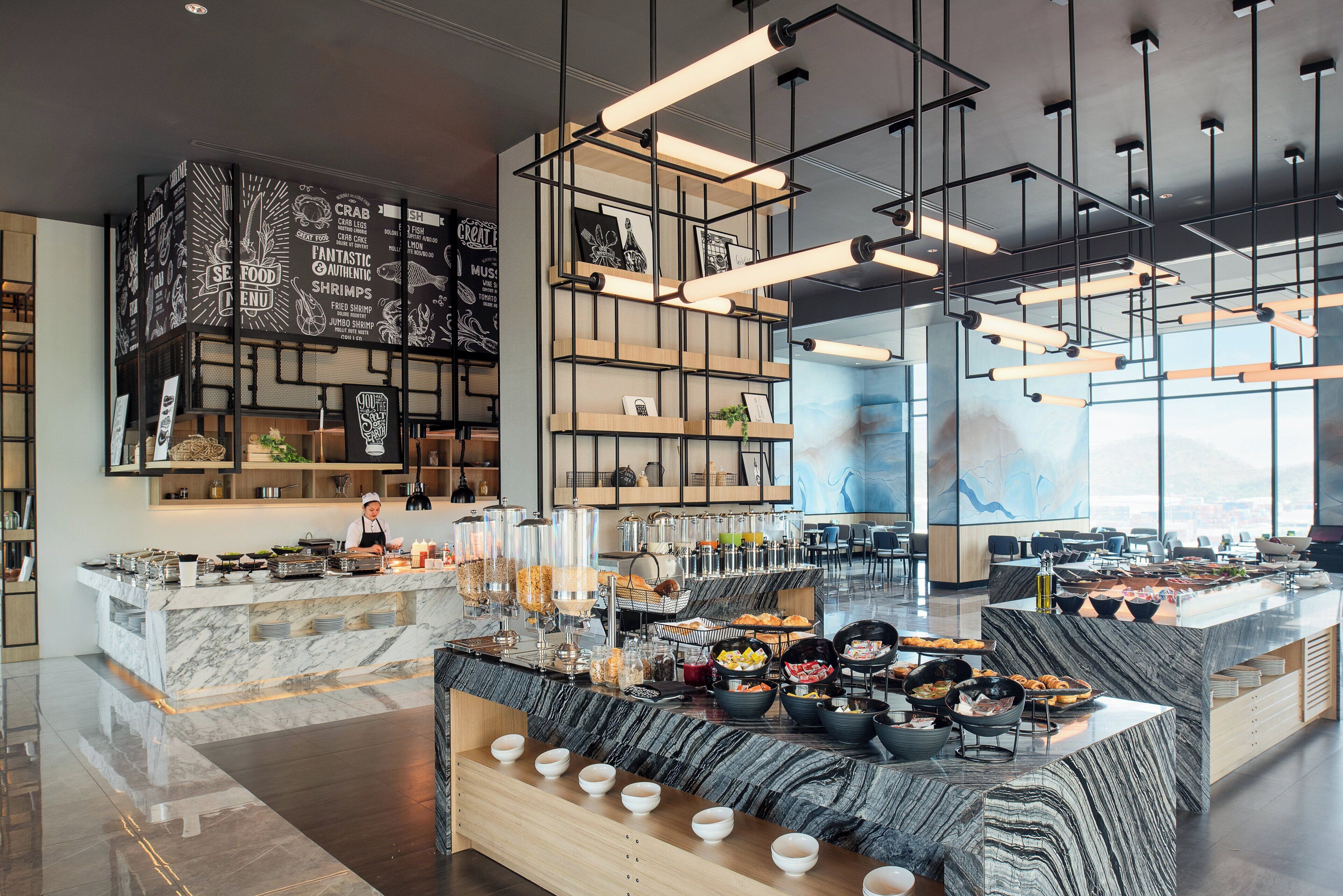 Un intérieur de restaurant moderne avec un comptoir central, un espace repas et un chef en pleine préparation.