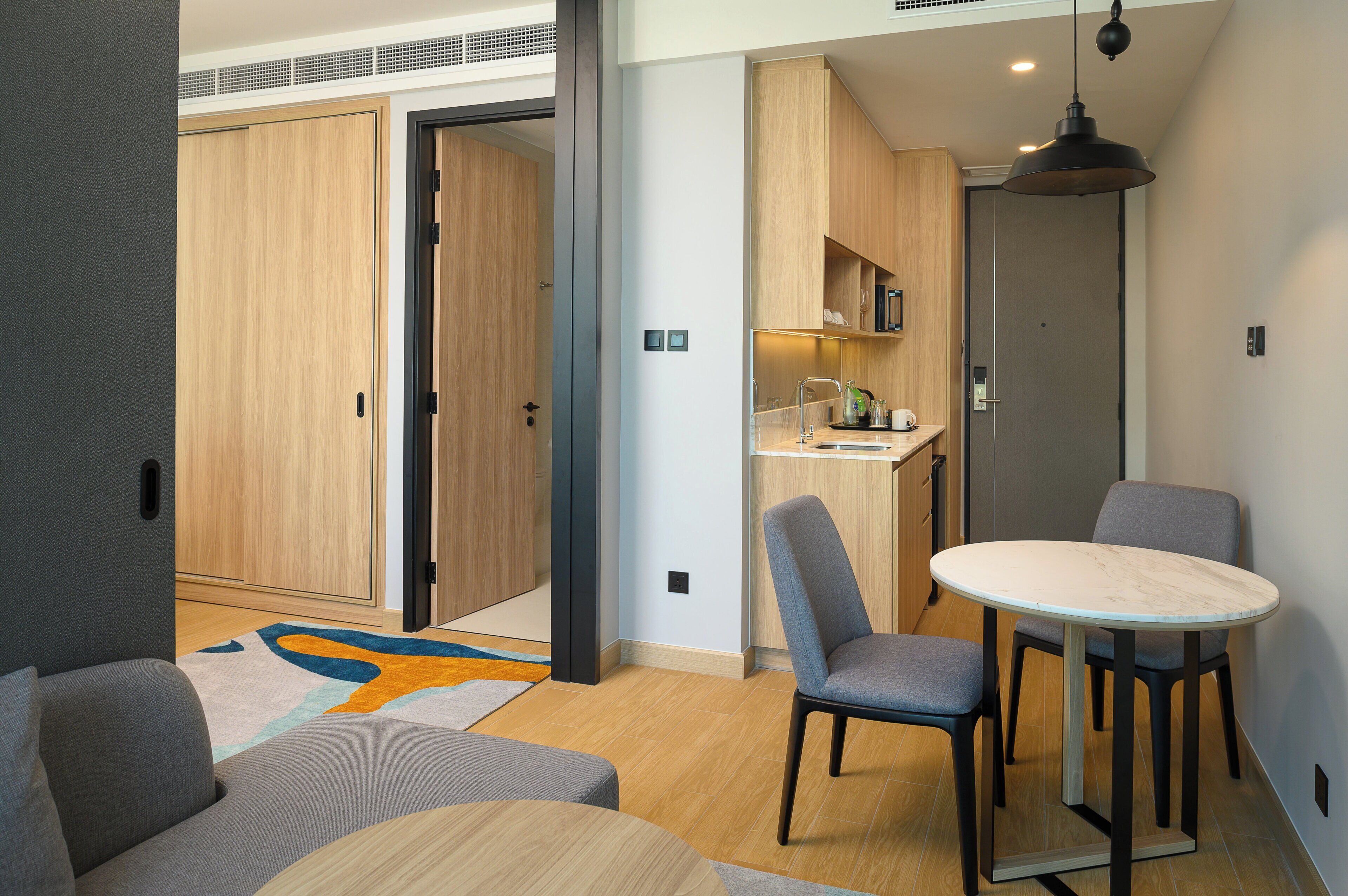 A modern hotel room with a dining area, kitchenette, and a large wardrobe.