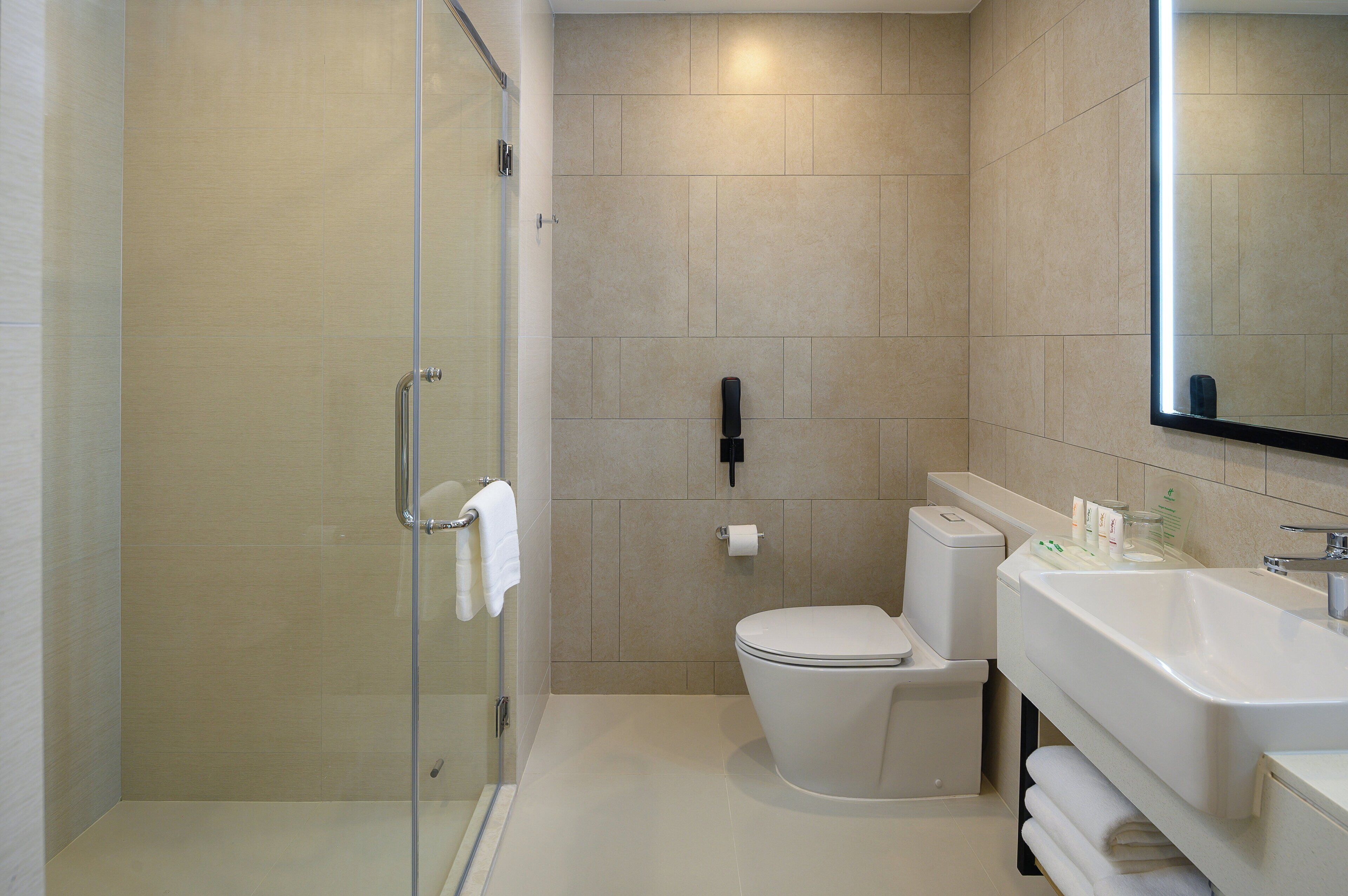 Une salle de bain moderne avec une douche à parois de verre, des toilettes blanches et un grand lavabo avec un miroir au-dessus.