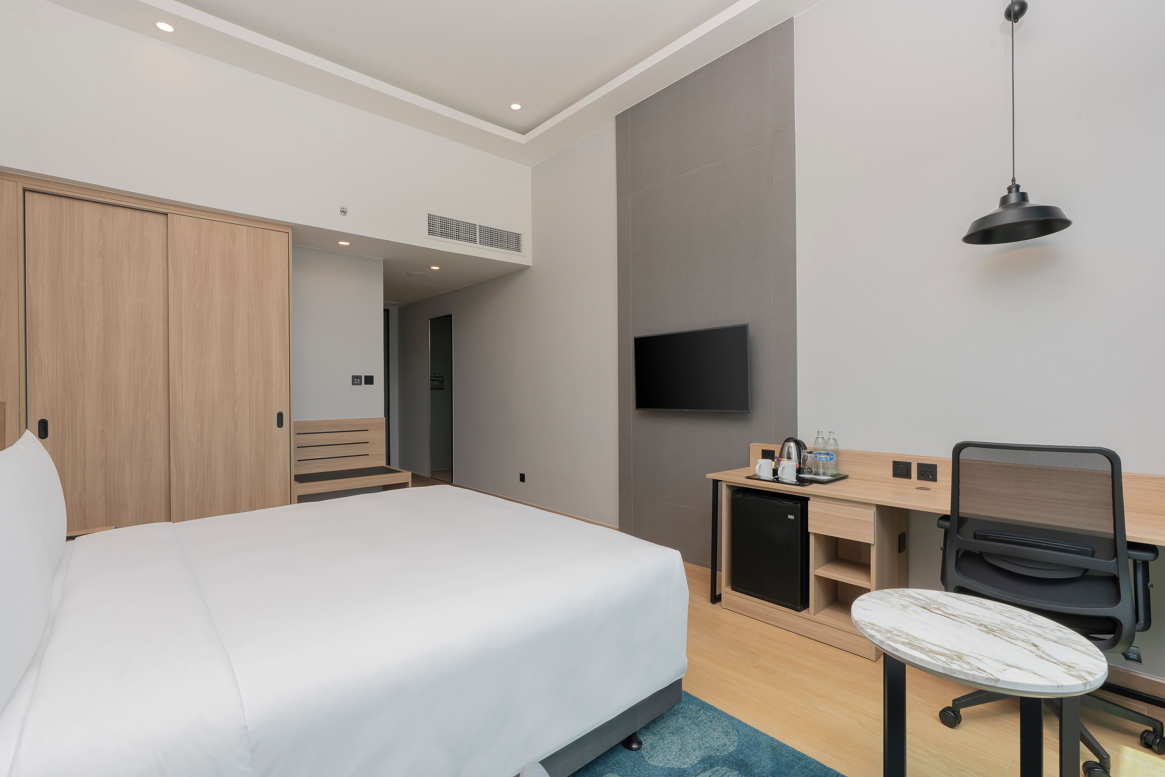 A hotel room with a bed, desk, chair, TV, and a small kitchenette.