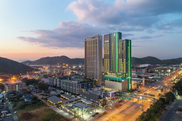 A high-rise hotel with multiple floors, surrounded by a cityscape with roads and other buildings. - Holiday Inn & Suites Siracha Laemchabang by IHG (Si Racha)