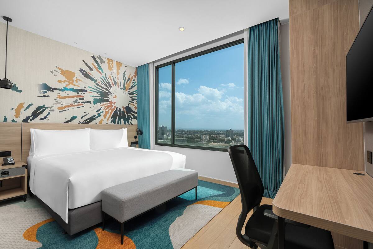 Une chambre d’hôtel avec un grand lit, un bureau et une vue sur la ville grâce à une grande fenêtre.