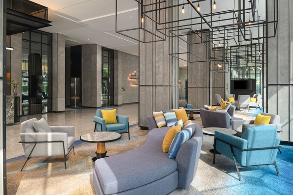 A modern lobby with a mix of seating options, including sofas and armchairs, arranged around a central area with a flat-screen TV. - Holiday Inn & Suites Siracha Laemchabang by IHG (Si Racha)