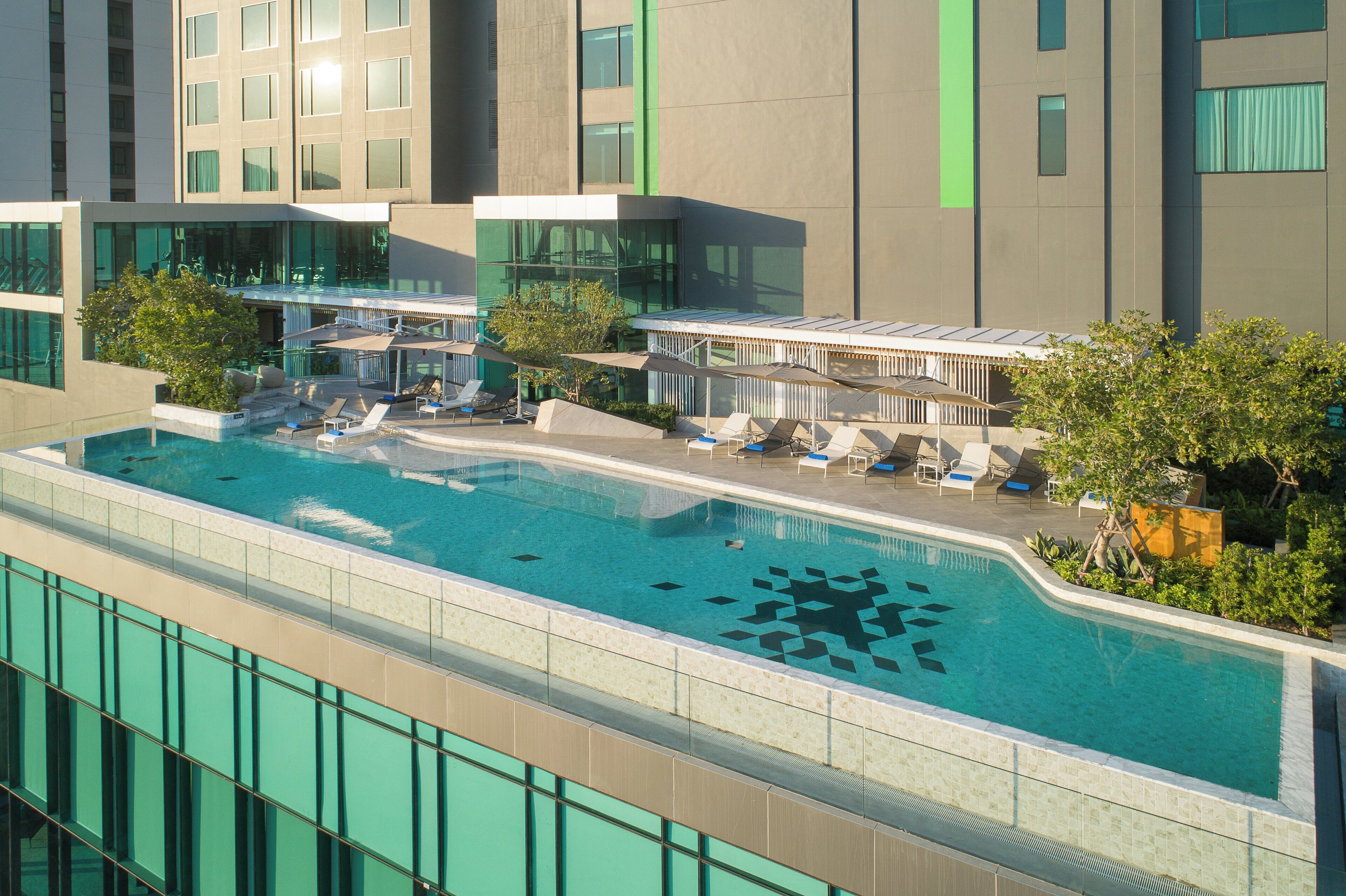 Et moderne hotel med en tagpool, liggestole og en glaskonstruktion.