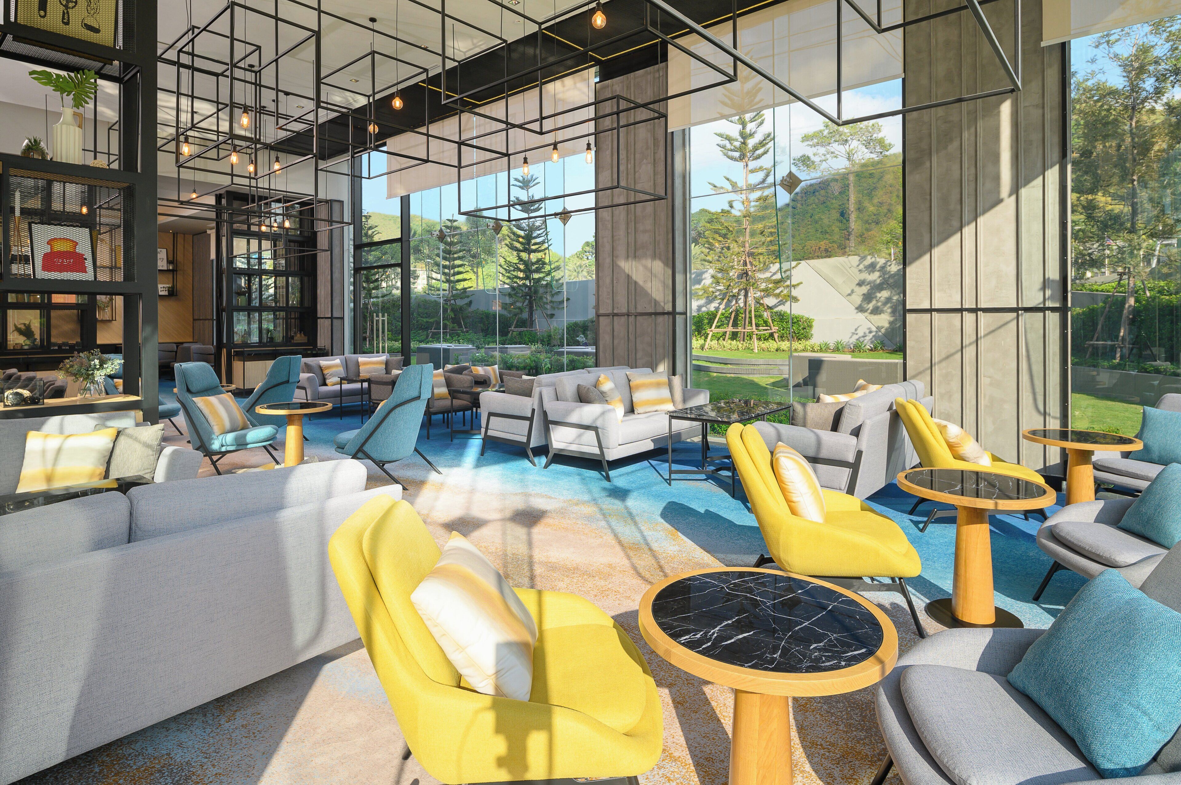 A modern lounge area with sofas, chairs, and tables, large windows offering a view of the outdoors.