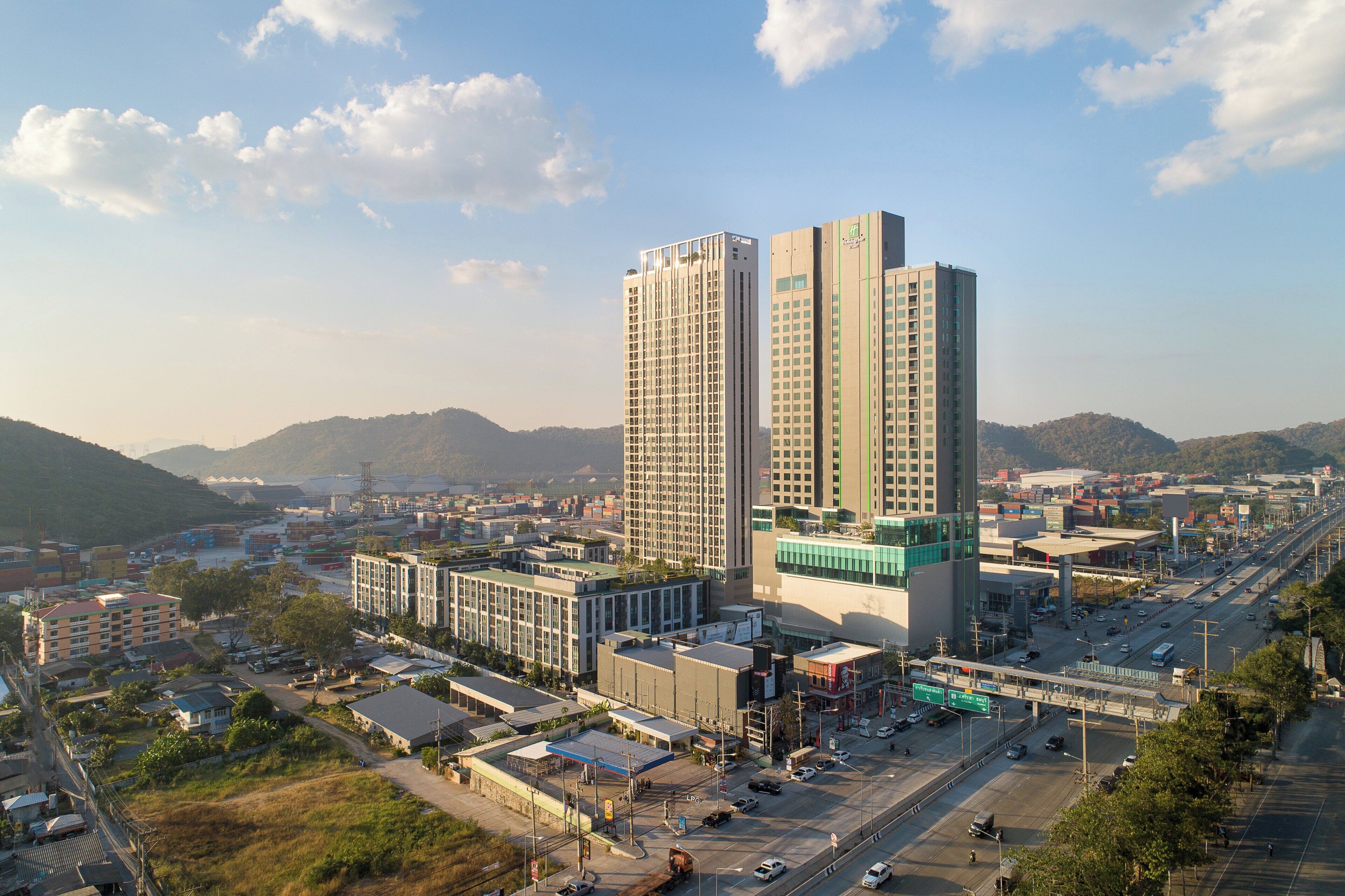 A high-rise building with multiple floors, surrounded by a commercial area with various shops and a highway.
