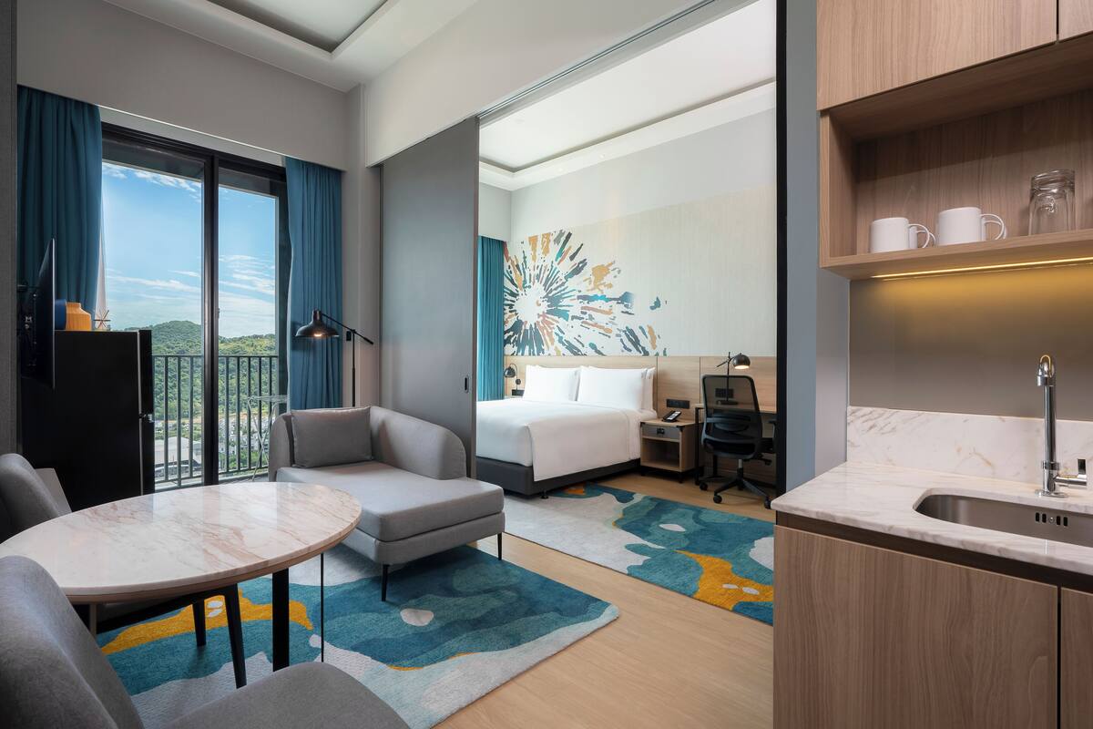 Une chambre d’hôtel moderne équipée d’un lit, d’un bureau, d’un canapé, d’une table à manger et offrant une vue sur l’extérieur.