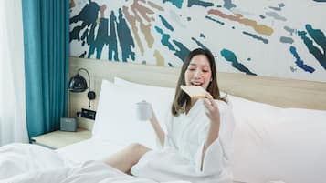A hotel room with a bed, a tray with breakfast items, and a wall with a colorful abstract design.