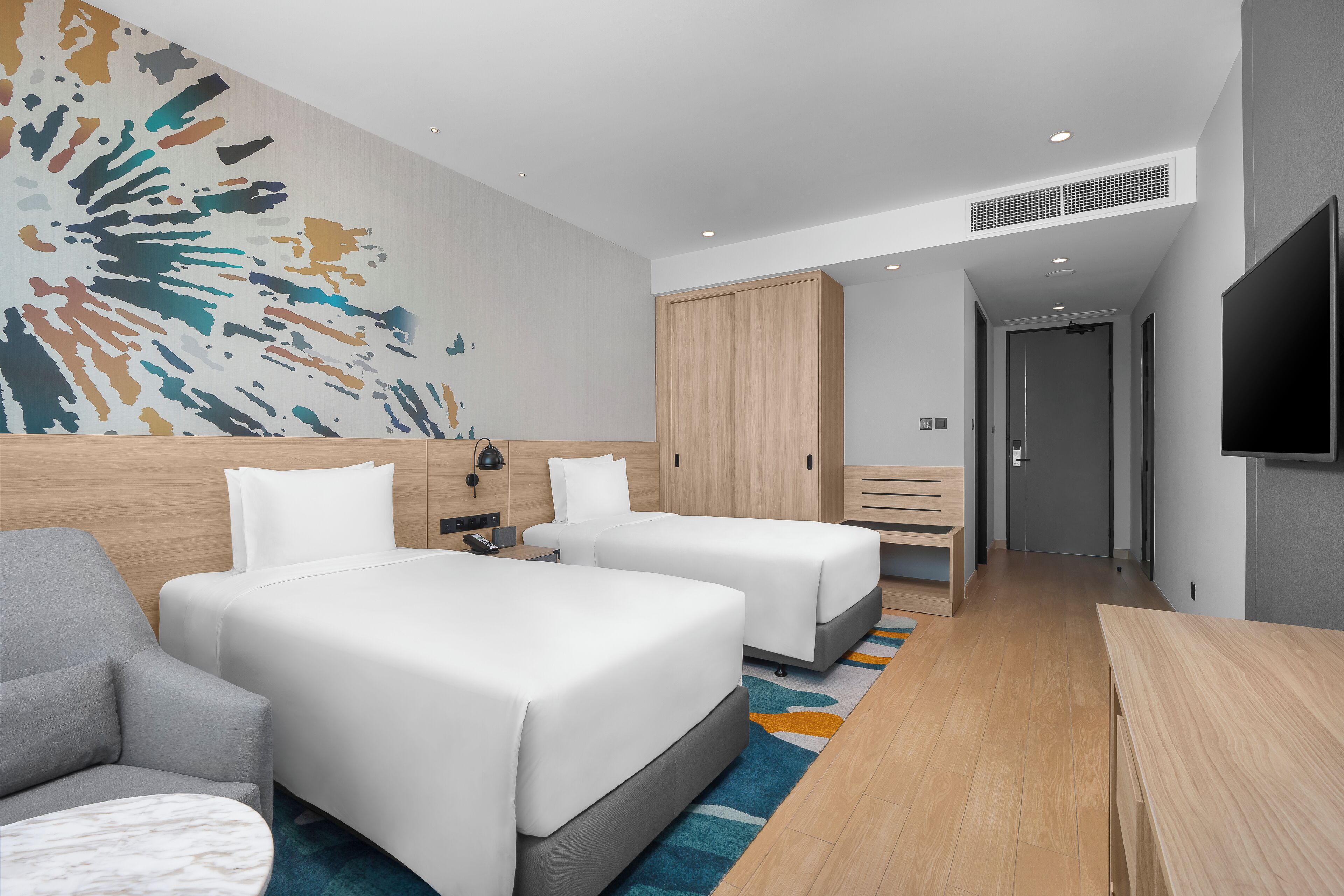 Ein modernes Hotelzimmer mit zwei Betten, einer Couch, einem Schreibtisch und einem großen abstrakten Wandbild.