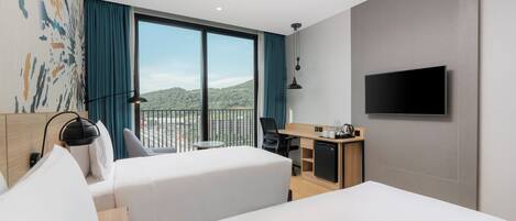 Une chambre d’hôtel dotée d’une grande fenêtre, d’un téléviseur à écran plat, d’un bureau et d’un lit.