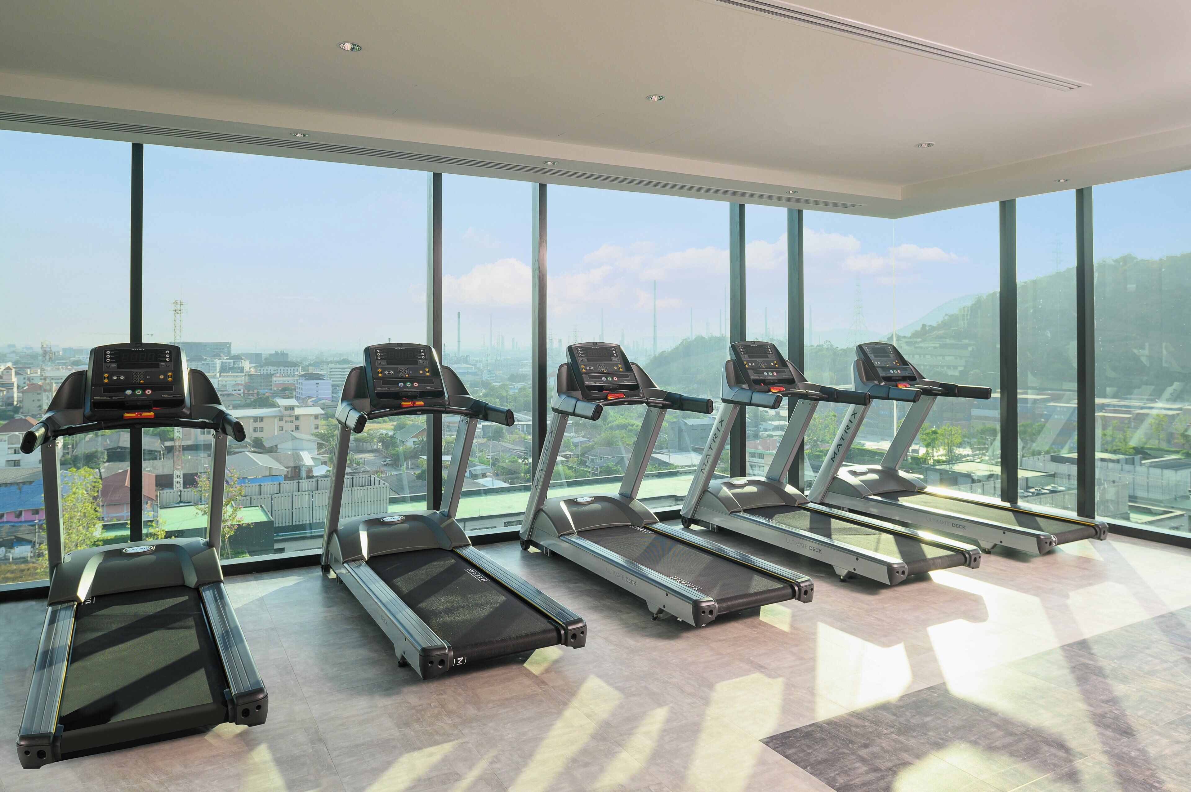 Ein Fitnessstudio mit Laufbändern und großen Fenstern mit Blick auf eine Stadtlandschaft.