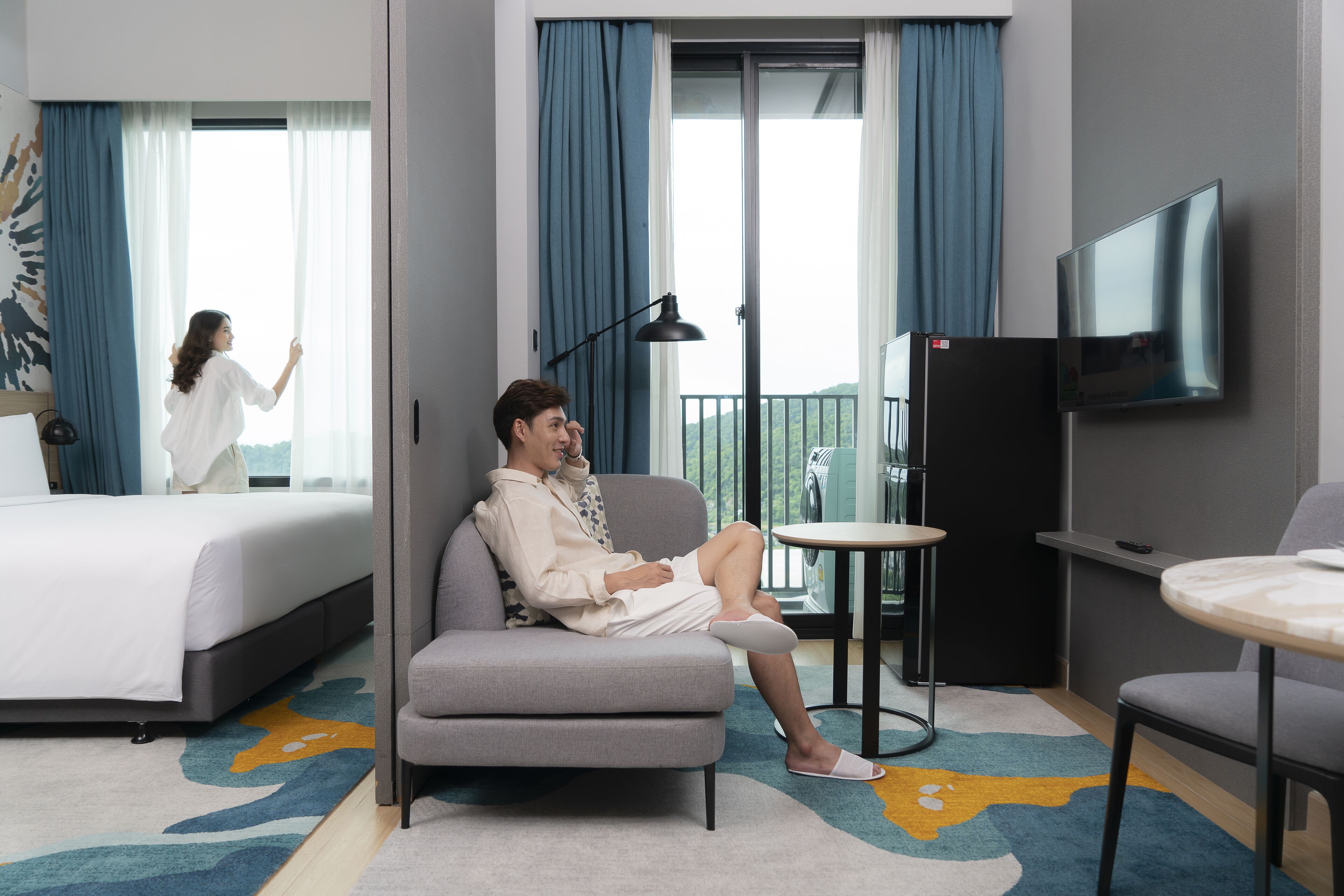 Une chambre d’hôtel comprenant un lit, un canapé, une petite table, une télévision et un balcon avec des rideaux.
