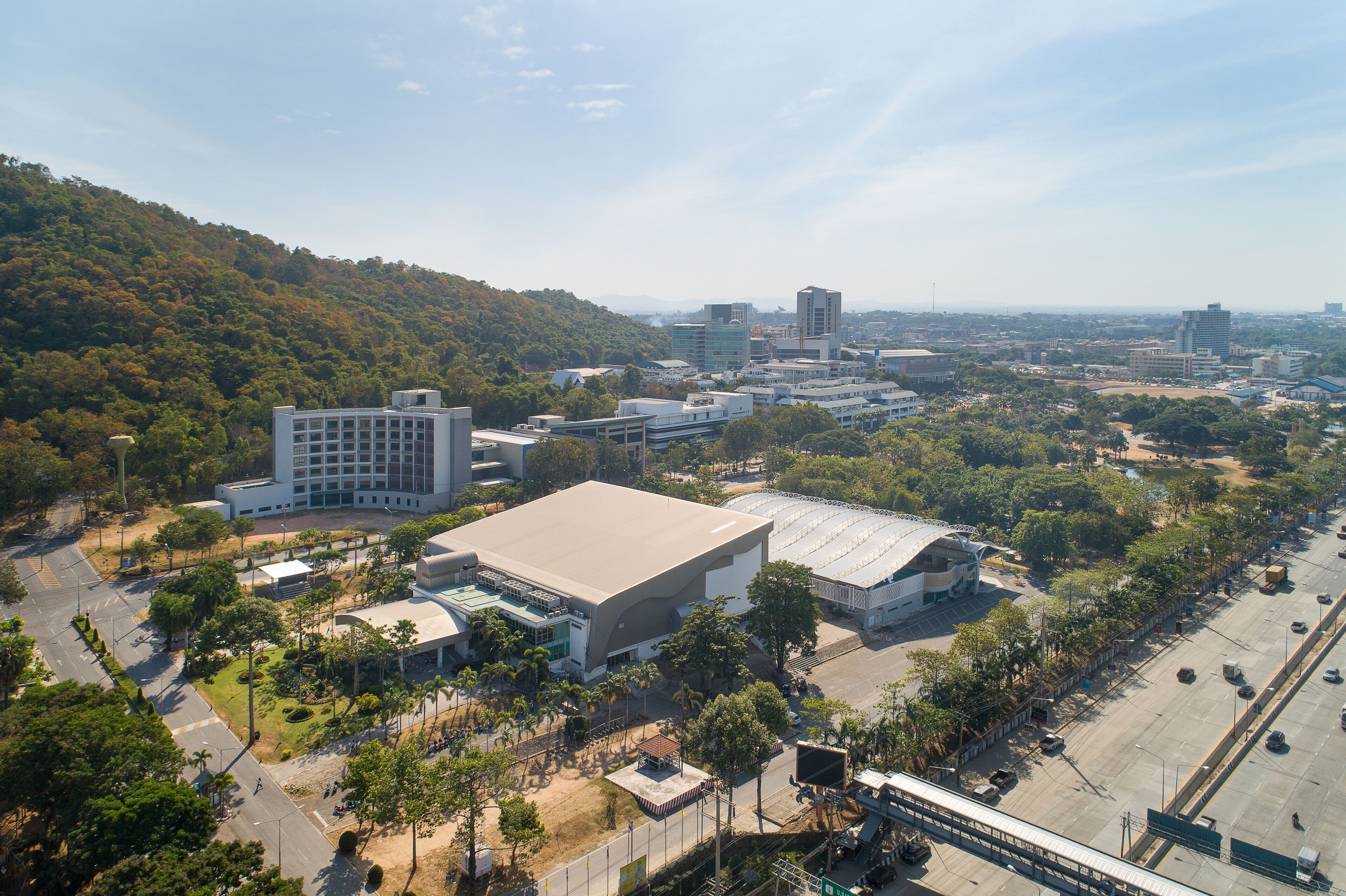 An aerial view of a cityscape with modern buildings, a large stadium, and surrounding greenery.