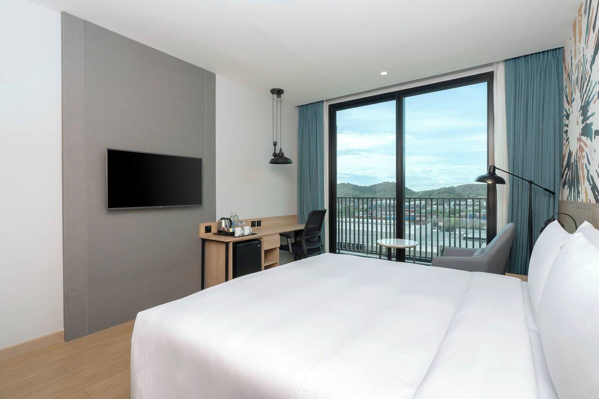 Une chambre d’hôtel équipée d’un lit, d’un bureau, d’une chaise, d’une télévision et d’un balcon avec vue.