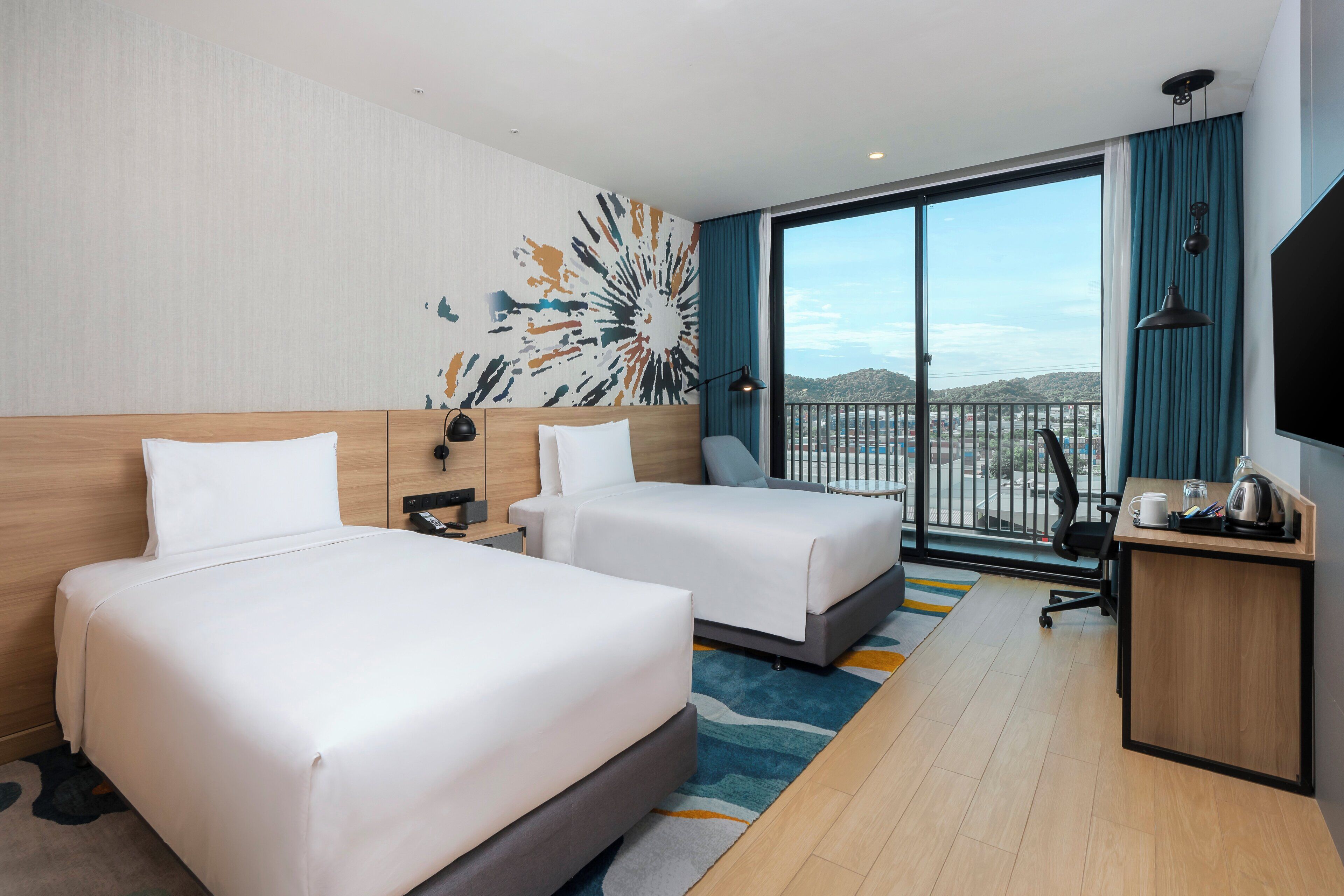 Une chambre d’hôtel avec deux lits, un bureau, une télévision et une grande fenêtre donnant sur un beau paysage.