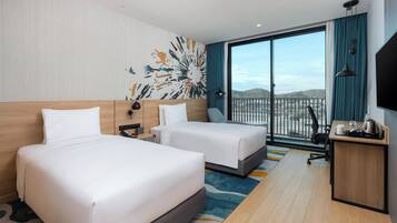 A hotel room with two beds, a desk, a TV, and a large window with a view.