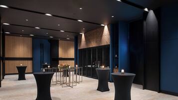 A modern hotel lobby with multiple tables and chairs, a reception desk, and a large wooden panel wall.
