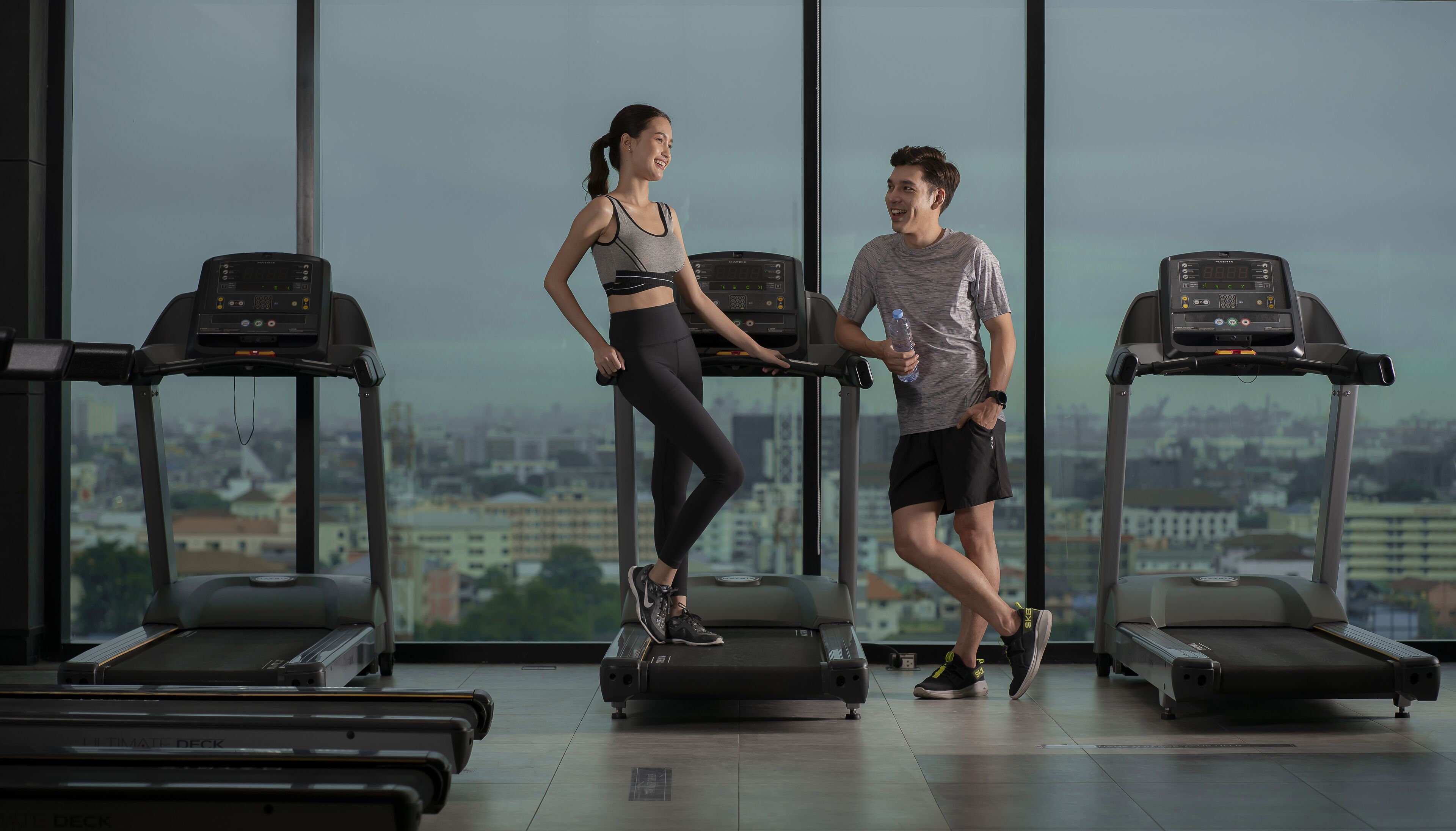Un gimnasio con cintas de correr, vistas a la ciudad y un ventanal grande.
