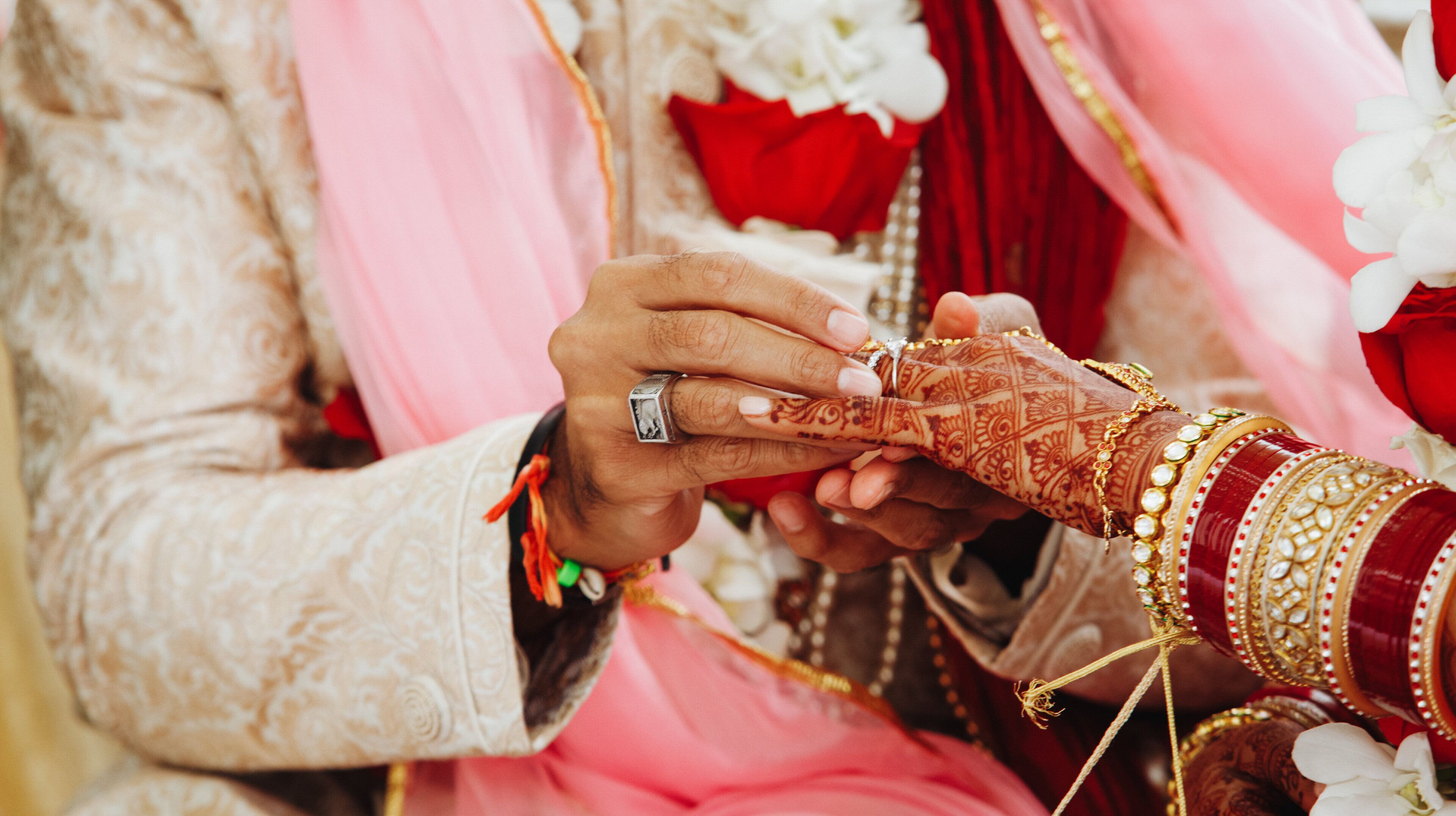 A close-up of hands exchanging rings, with intricate henna designs and traditional jewelry.