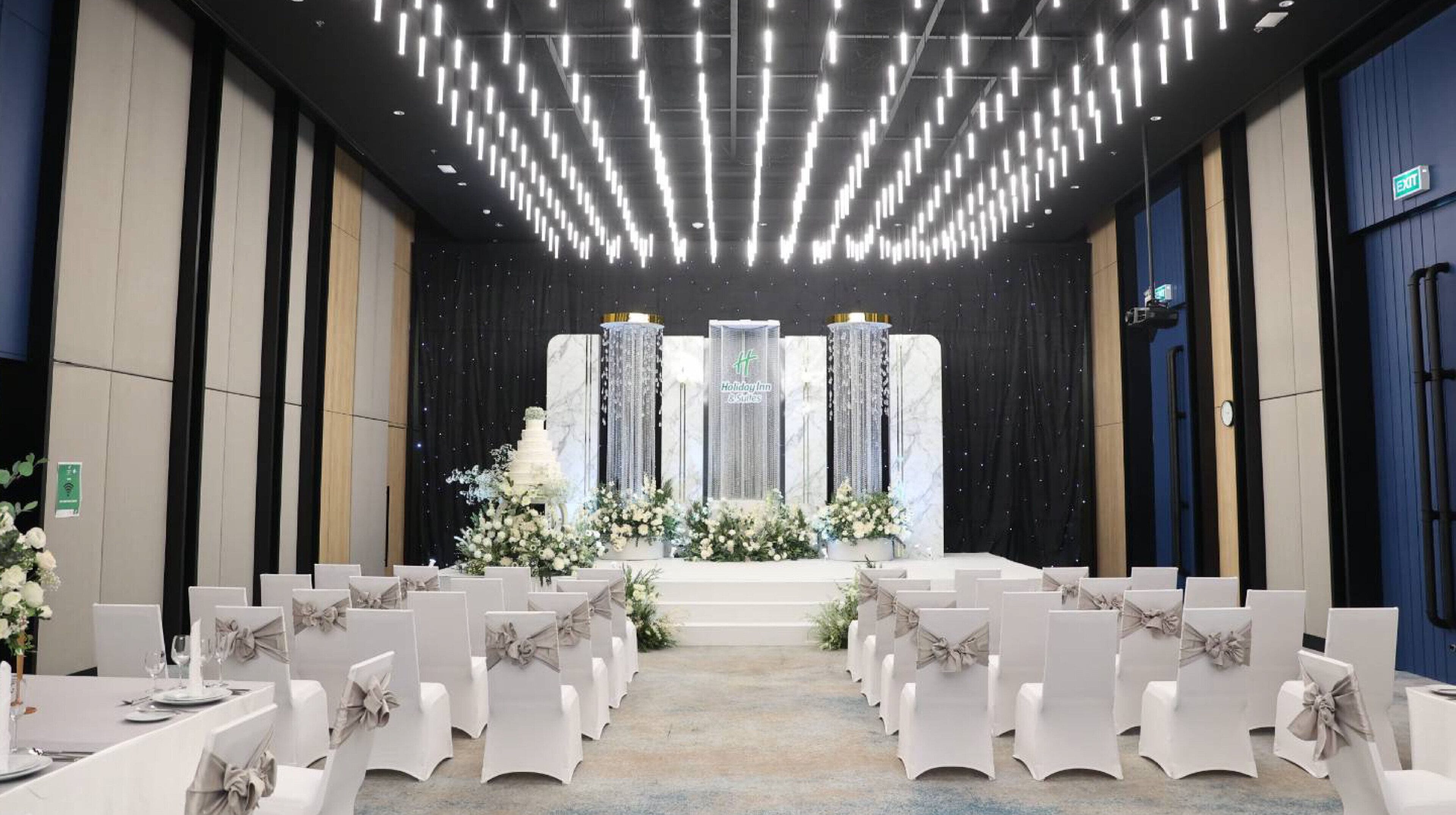 A hotel interior with a stage, rows of white chairs, and a modern chandelier.
