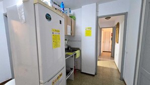 A compact kitchen with a refrigerator, a sink, and a countertop. There are two yellow warning signs on the walls. - Low Cost Room Las Llaves 3 (San Bartolomé de Tirajana)