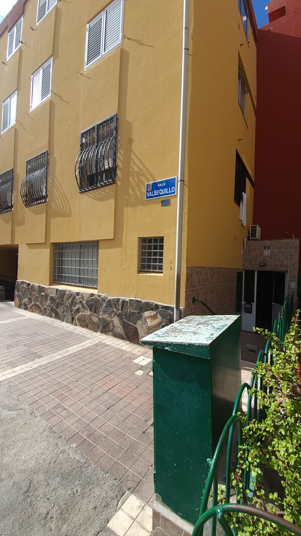 Un bâtiment jaune avec un socle en pierre, un panneau de rue bleu indiquant « Calle Valsequillo », et une poubelle verte.