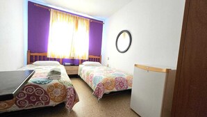 A small, clean room with two beds, a small table, a mirror, and a window with curtains. - Low Cost Room Las Llaves 3 (San Bartolomé de Tirajana)