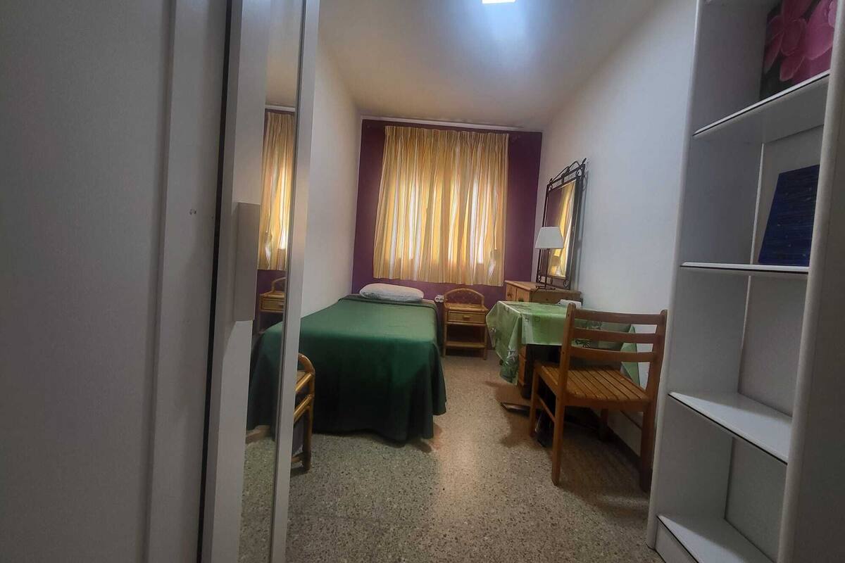 A small, compact room with two single beds, a desk, a chair, and a wardrobe.