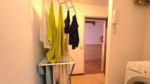 A laundry area with a drying rack, a washing machine, and a door leading to another room. - Low Cost Room Las Llaves 3 (San Bartolomé de Tirajana)