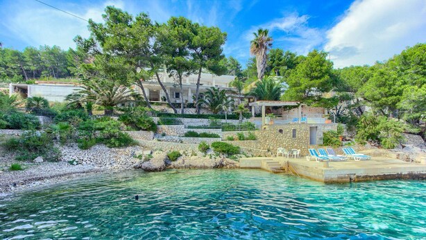 Une propriété située sur la côte, dotée d’une piscine à eau claire, d’un escalier en pierre menant à une terrasse et offrant une vue sur la mer.